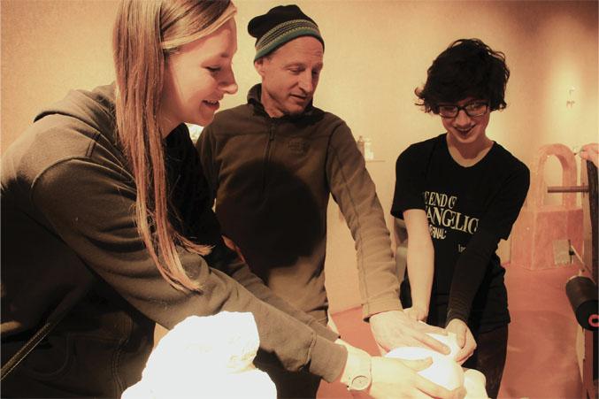 Paige Rajms, Bill Cravis and Kira Davis gather around Davis's sculpture made of plaster named "Fondle with Care."