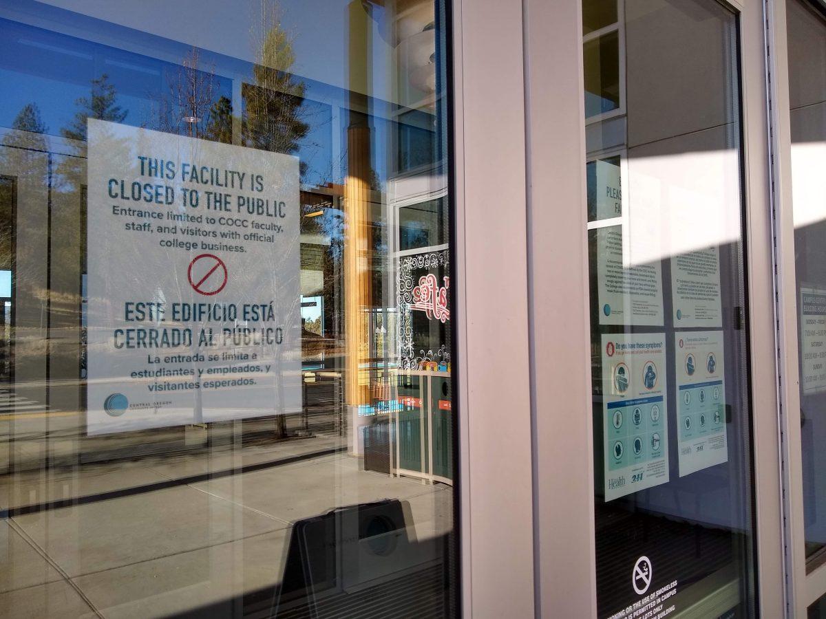 A number of signs are posted to a door notifying that the COCC campus is closed due to the COVID-19 pandemic.
