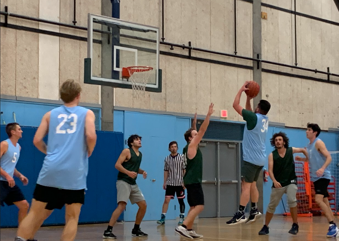 Student wearing light blue jersey jumps to shoot the basketball over a student wearing a dark jersey.