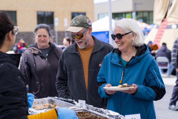 People stand in line and smile while their plate is loaded with food.