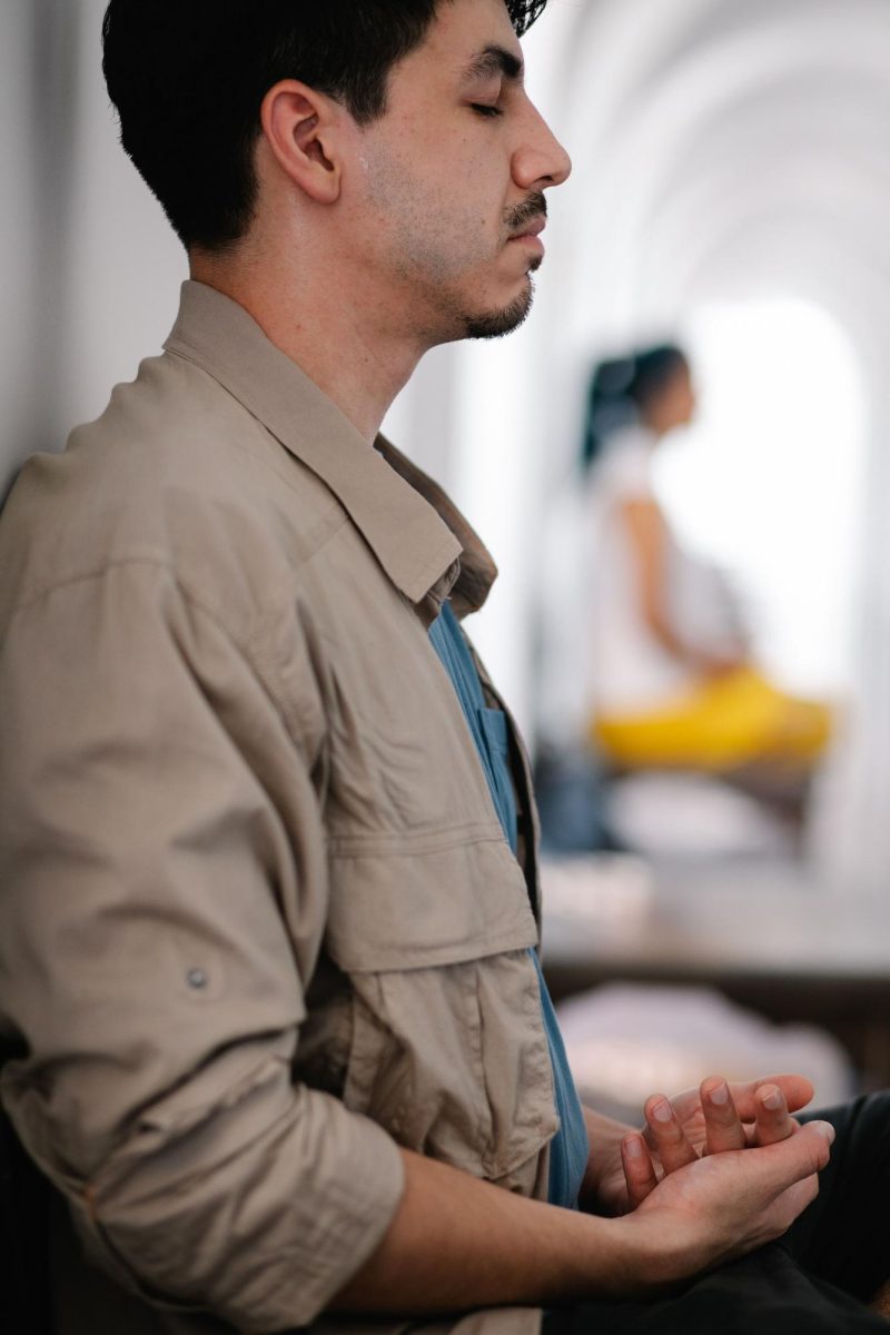A man sits with his eyes closed and his hands opened in his lap, in contemplation or prayer.