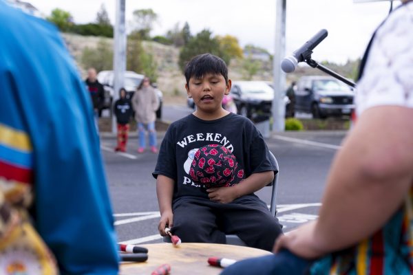 A child sings and drums, with other people, on a communal drum.