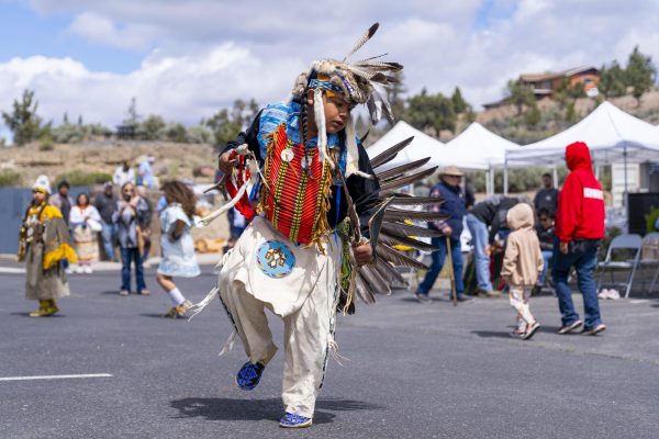 A youth in feathered and beaded Native American clothing performs a traditional dance.