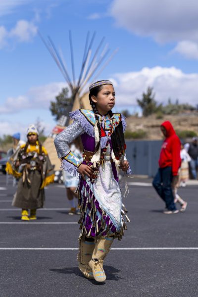 A child in fringed and beaded Native American regalia dances in a parking lot.