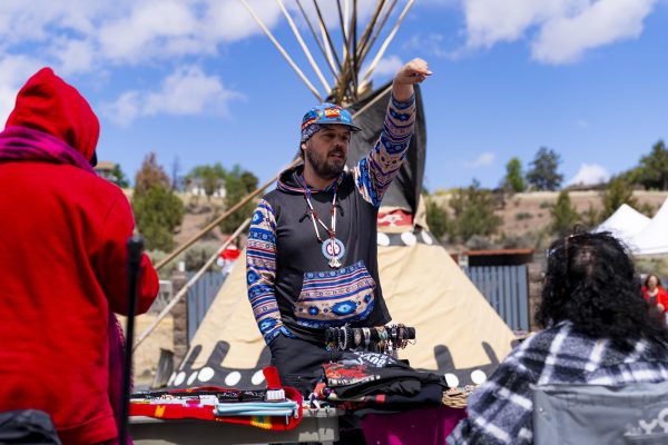 A man stands at a vendor booth and points, with a teepee behind him.