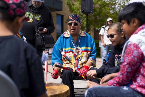Several Native American people sit around a large drum and sing.
